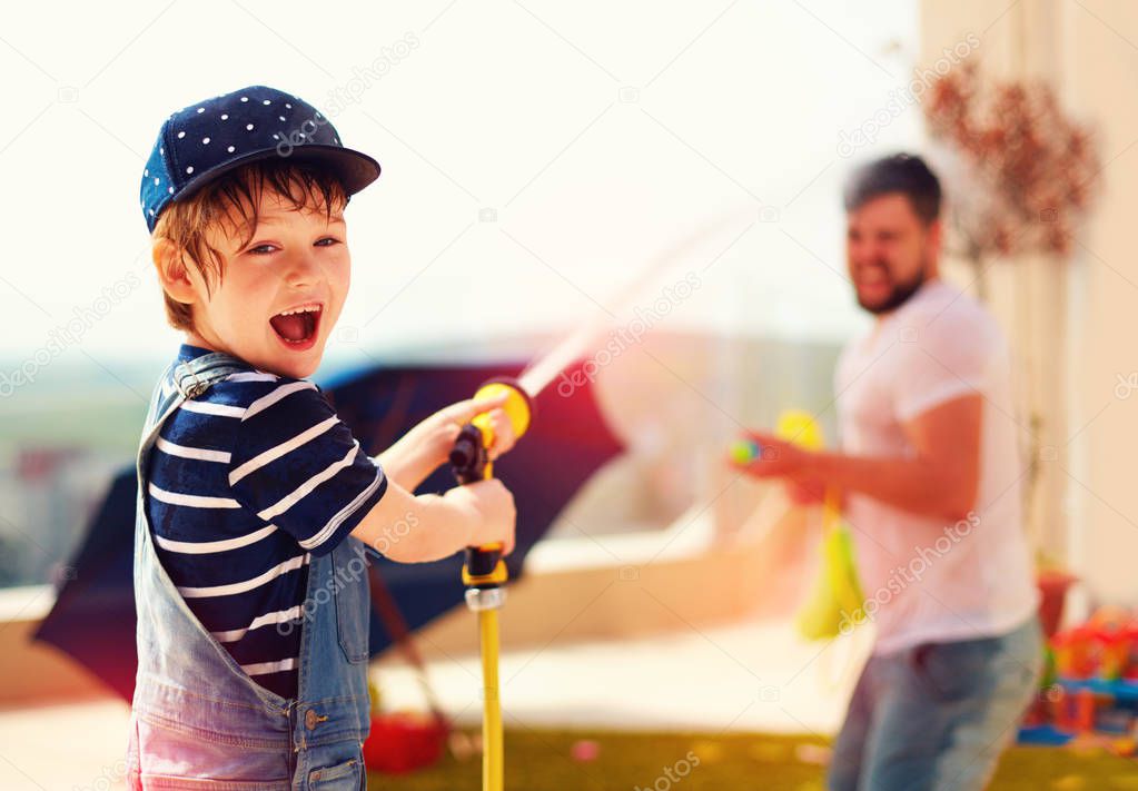 excited young boy having fun, splashing water with father at warm summer day