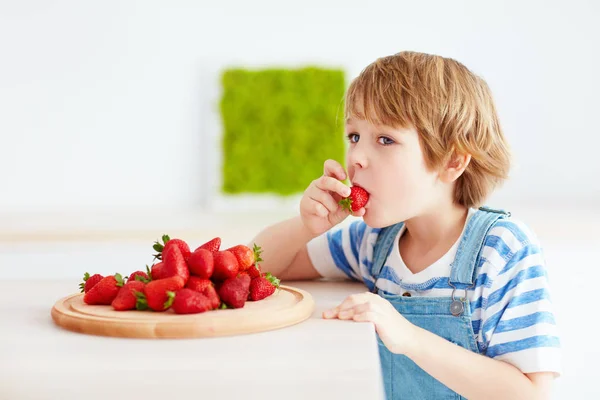 Милый счастливый ребенок ест вкусную спелую клубнику на кухне — стоковое фото
