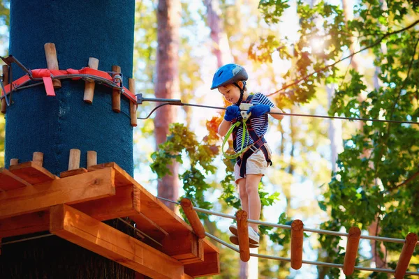 Chico joven pasando la ruta de cable alto entre los árboles, deporte extremo en parque de aventuras — Foto de Stock