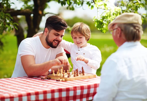 Happy family of three generation of men playing chess in spring garden — Stock Photo, Image