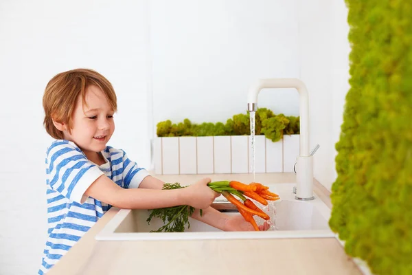 Lindo joven lavando las zanahorias bajo el agua del grifo en la cocina — Foto de Stock