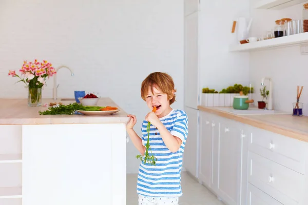 Lindo niño, chico comiendo sabrosa zanahoria fresca en la cocina — Foto de Stock