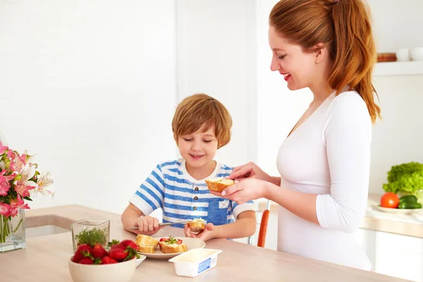 Mãe feliz e filho preparando lanches pela manhã na cozinha em casa — Fotografia de Stock