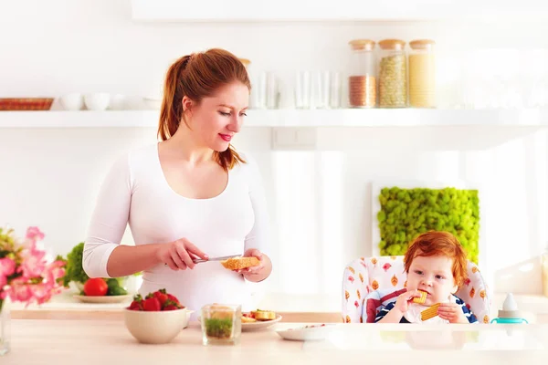 Junge Mutter mit Säugling im Hochstuhl beim Frühstück in der Küche — Stockfoto