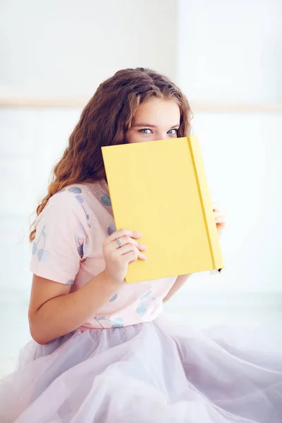 Hermosa joven escondiendo la cara detrás del libro — Foto de Stock