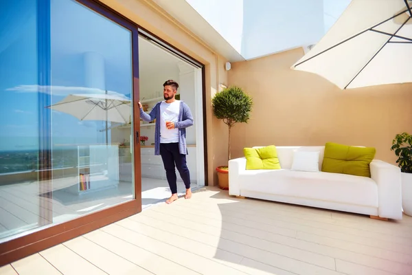 Handsome man enjoys life on rooftop terrace, with open space kitchen and sliding doors — Stock Photo, Image