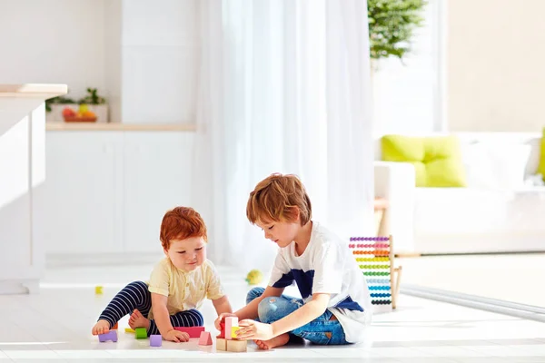 Fratello maggiore che gioca con il bambino in mattoni di legno colorati, a casa — Foto Stock