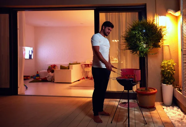 Hombre adulto joven preparando comida para la familia en el patio de la noche en ho — Foto de Stock