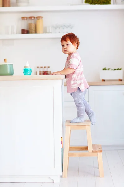 Baby cute maluch wspina się na stołek, stara się osiągnąć wysoką nosorożca w kuchni — Zdjęcie stockowe