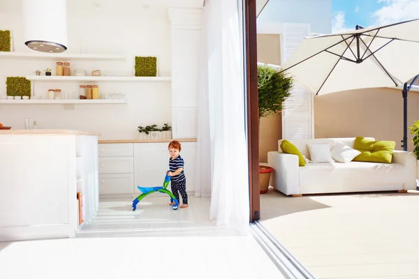 Um bebê criança andando com go-cart na cozinha de espaço aberto e pátio no último piso com portas de correr — Fotografia de Stock