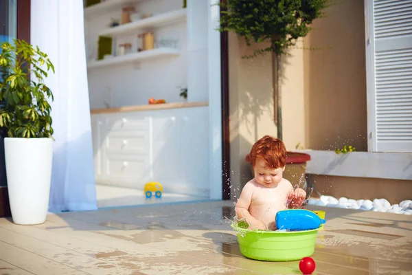 Cute redhead toddler baby having fun with water on summer terrace — Stock Photo, Image