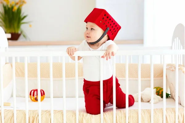 Bebê engraçado com cesta de brinquedo como capacete estão em seu berço — Fotografia de Stock