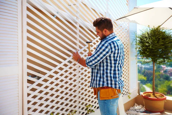 Giovane uomo adulto decorare la parete della casa, con la creazione del traliccio di legno per piante rampicanti — Foto Stock