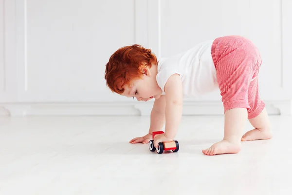 Lindo pelirrojo bebé niño rodando un juguete coche en el suelo — Foto de Stock