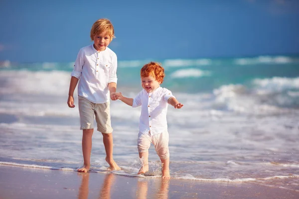 Giovane ragazzo giocare con junior fratello su sabbia spiaggia — Foto Stock