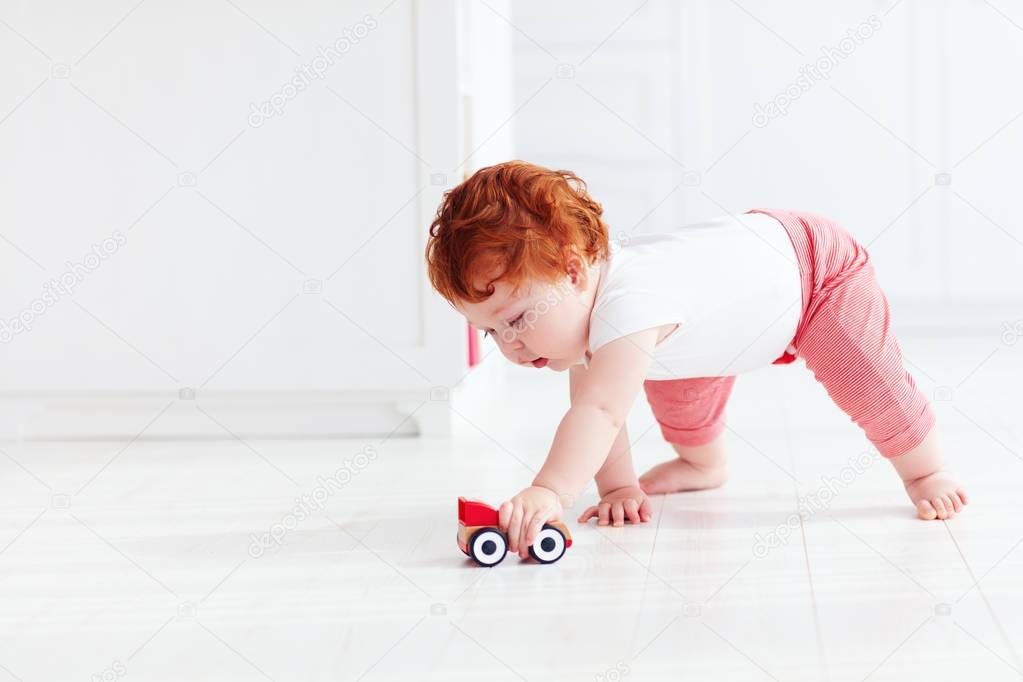 cute redhead baby boy rolling a toy car on the floor