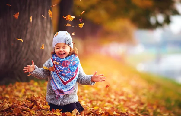 Entzückendes glückliches Mädchen, das im Herbstpark mit fallenden Blättern spielt — Stockfoto
