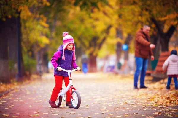 Carino felice ragazza in sella a una bicicletta in autunno strada — Foto Stock