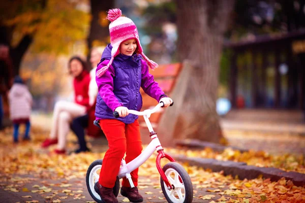 Carino felice ragazza in sella a una bicicletta in autunno strada — Foto Stock