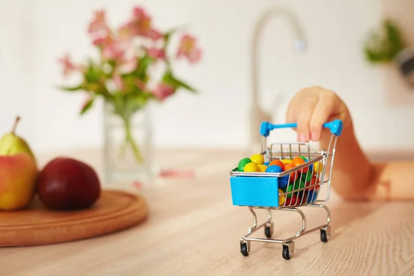 Mini shopping trolley full of candies on kitchen desk — Stock Photo, Image