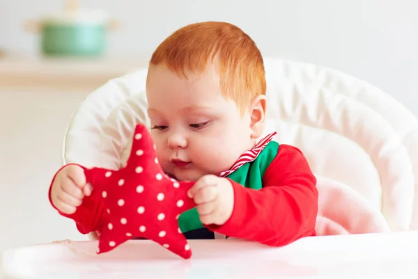 Cute infant redhead baby boy in elf costume playing with red star in highchair — Stock Photo, Image