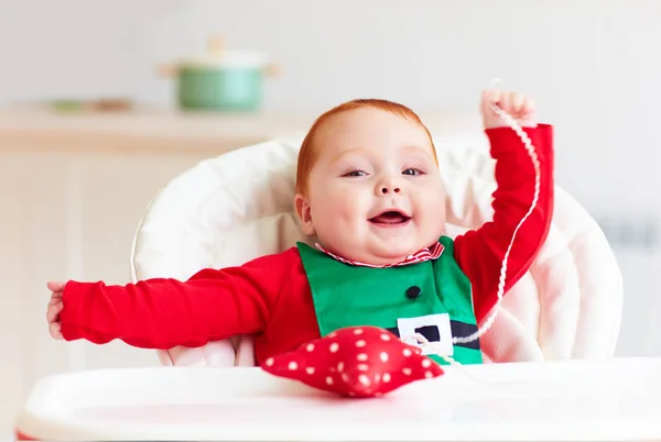 Niedliches rothaariges Baby im Elfenkostüm, das mit rotem Stern im Hochstuhl spielt — Stockfoto