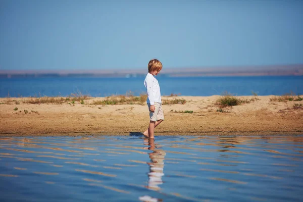 反射水で湖岸を歩いてかわいい少年 — ストック写真