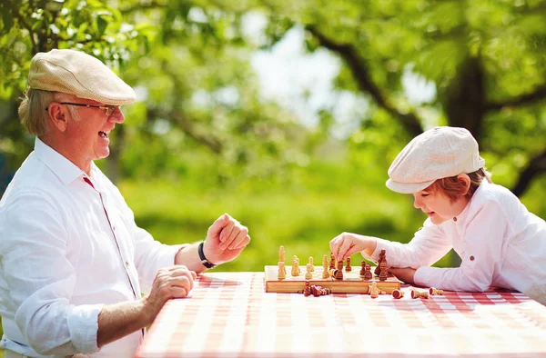 Happy grandpa and grandson playing chess in spring garden — Stock Photo, Image