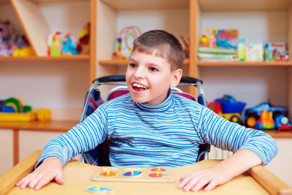 Fröhlicher Junge mit Behinderung im Rehabilitationszentrum für Kinder mit besonderen Bedürfnissen, Lösen logischer Rätsel — Stockfoto