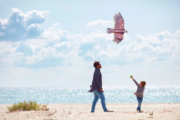 Alegre padre e hijo, familia lanzando la cometa en la playa de arena, en el día ventoso —  Fotos de Stock