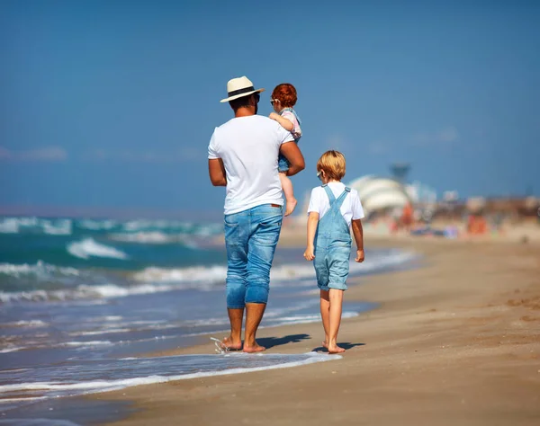 Vista trasera de la familia, padre con niños caminando en la playa de arena cerca del mar, vacaciones de verano —  Fotos de Stock
