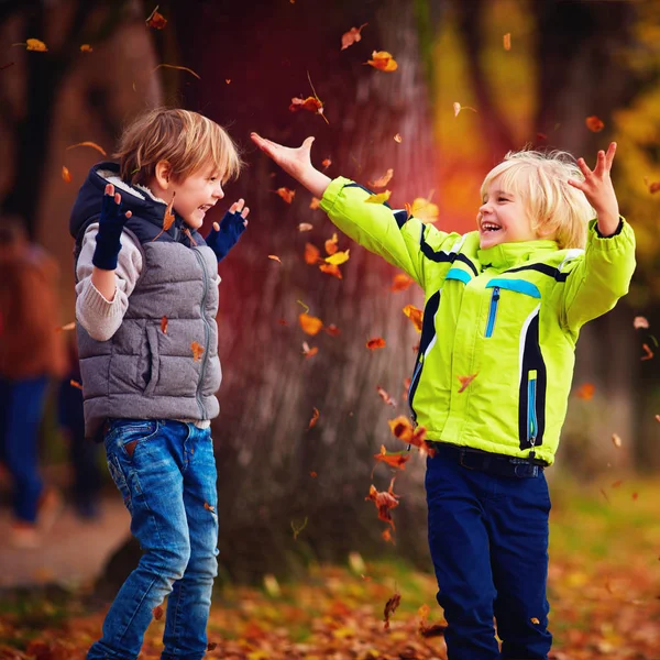Задоволені щасливі школярі розважаються кидаючи опале листя в осінній парк — стокове фото
