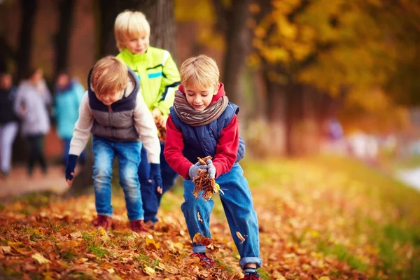 Happy school kids, friends having fun throwing fallen leaves up in autumn park — Stock Photo, Image