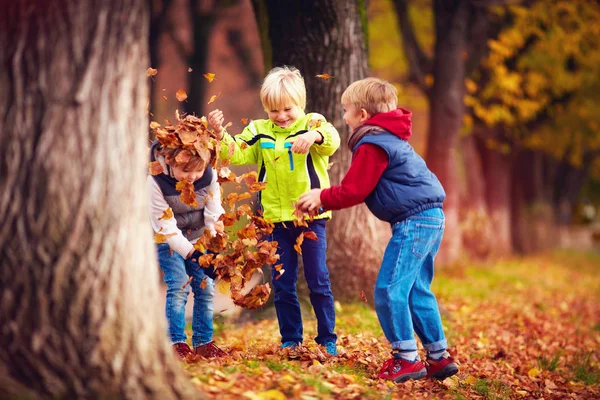 Delighted happy school kids, friends having fun throwing fallen leaves in autumn park — Stock Photo, Image