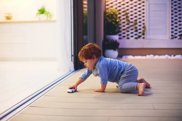 Bonito criança bebê menino brincando com brinquedo carro no pátio com espaço aberto cozinha e portas de correr — Fotografia de Stock