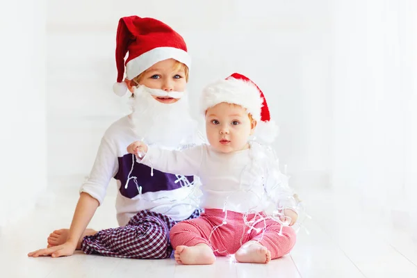 Schattig broer broers en zussen, kinderen in santa's hoeden en garland spelen thuis — Stockfoto