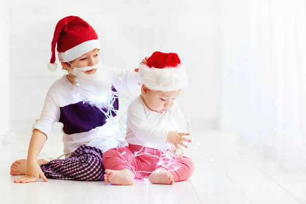 Schattig broer broers en zussen, kinderen in santa's hoeden en garland spelen thuis — Stockfoto