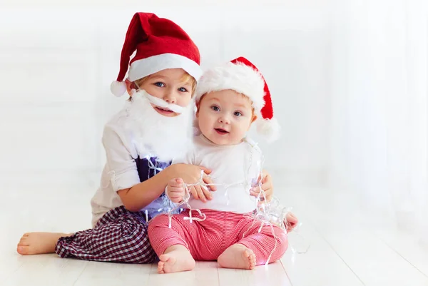 Cute brother siblings, kids in santa's hats and garland playing at home — Stock Photo, Image