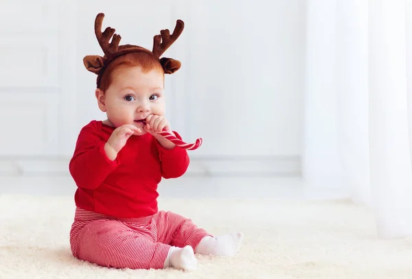 Cute little redhead baby boy with reindeer band tasting christmas sweet treats, sitting on the floor at home — Stock Photo, Image