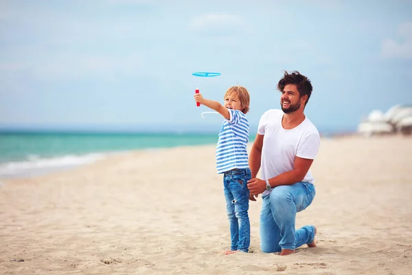 De lancering van de gelukkige vader en zoon plezier op het strand, het spelen van de spelen van de activiteit van de zomer, propeller speelgoed in de lucht — Stockfoto