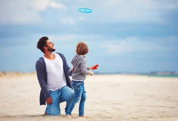 Feliz padre e hijo divirtiéndose en la playa, jugando juegos de actividades de verano, lanzamiento de juguetes de hélice en el aire — Foto de Stock