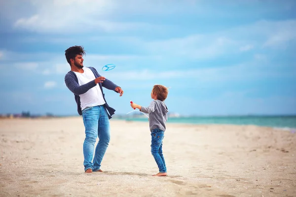 Happy father and son having fun on the beach, playing summer activity games, launching propeller toy in the air — Stock Photo, Image