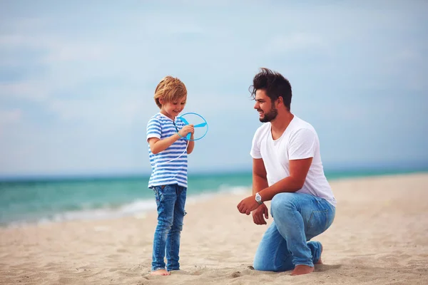 Feliz padre e hijo divirtiéndose en la playa, jugando juegos de actividades de verano, lanzamiento de juguetes de hélice en el aire —  Fotos de Stock