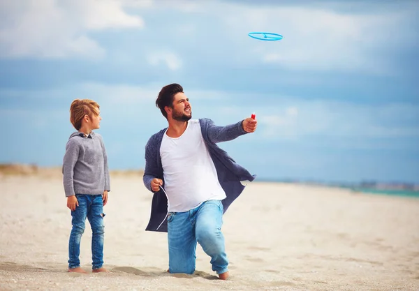 Happy father and son having fun on the beach, playing summer activity games, launching propeller toy in the air — Stock Photo, Image