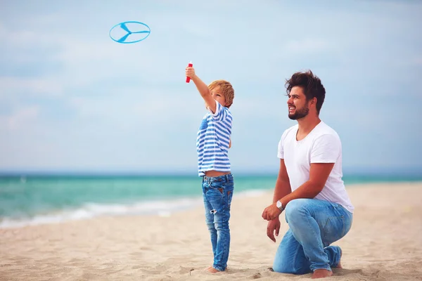 Felice padre e figlio divertirsi sulla spiaggia, giocare giochi di attività estive, lanciare il giocattolo dell'elica in aria — Foto Stock