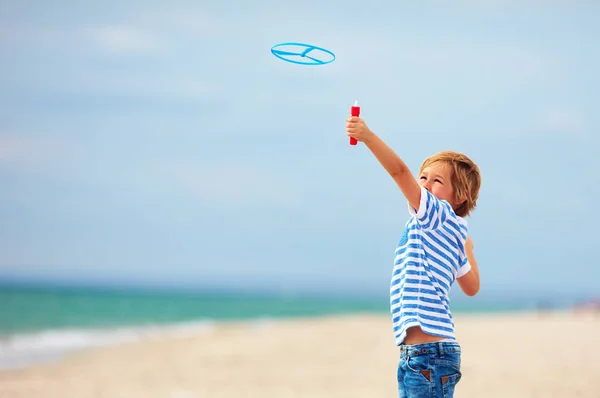 Delighted cute young boy, kid having fun on sandy beach, playing leisure activity games with propeller toy — Stock Photo, Image