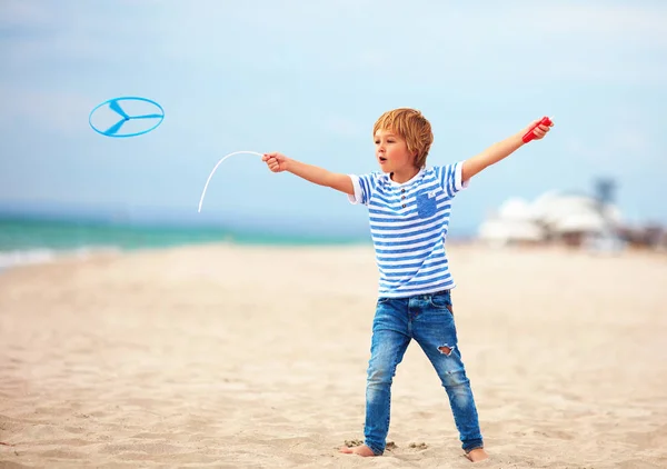 Delighted cute young boy, kid having fun on sandy beach, playing leisure activity games with propeller toy — Stock Photo, Image