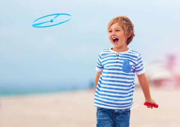 Encantado lindo niño, niño que se divierte en la playa de arena, jugando juegos de ocio con el juguete de la hélice —  Fotos de Stock