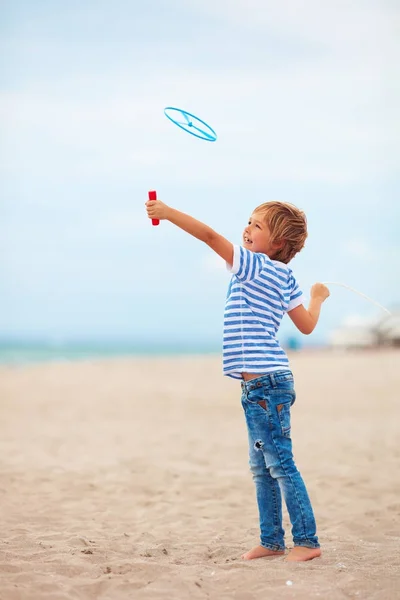 Delighted cute young boy, kid having fun on sandy beach, playing leisure activity games with propeller toy — Stock Photo, Image