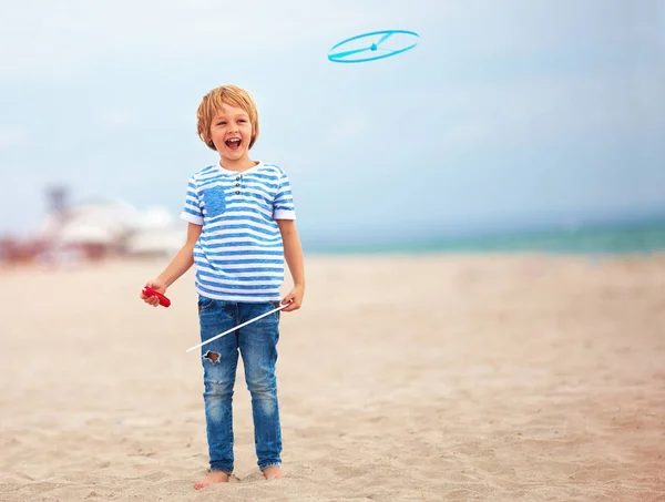 Восхитительный милый мальчик, ребенок, веселящийся на песчаном пляже, играющий в досуговые игры с пропеллером — стоковое фото